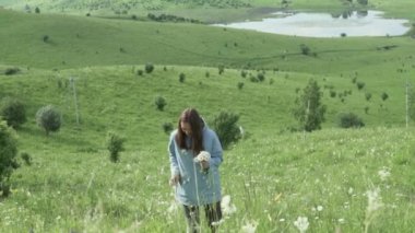 Bir kadın tarlada bir buket yabani çiçek toplar.