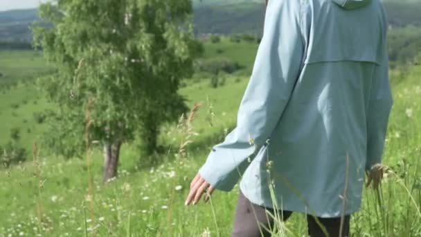 Een vrouw loopt op een groen veld met bloemen — Stockvideo