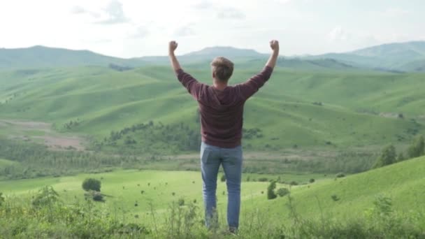 Человек поднимает руки, стоя на вершине горы утром — стоковое видео