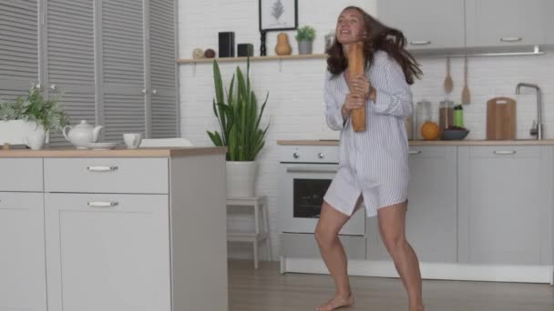 Eine junge Frau im Nachthemd tanzt fröhlich in der Küche mit einem Laib Brot — Stockvideo