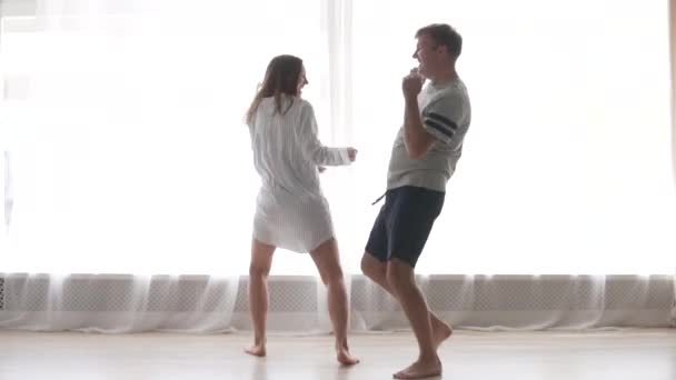 Χαρούμενο παντρεμένο ζευγάρι που χορεύει με τις πιτζάμες του στο παράθυρο το πρωί. — Αρχείο Βίντεο