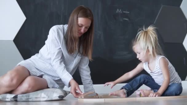 Moeder en haar kleine dochter bouwen aan een spoorweg thuis. — Stockvideo