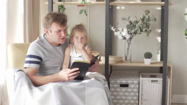 Pappa läser en bok till sin lilla dotter. — Stockvideo