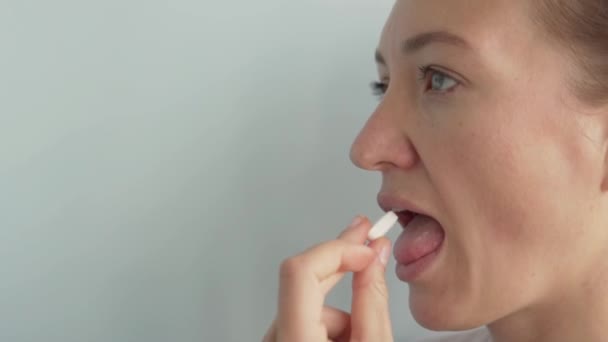 Una mujer traga una pastilla blanca grande y la bebe con agua de un vaso — Vídeo de stock