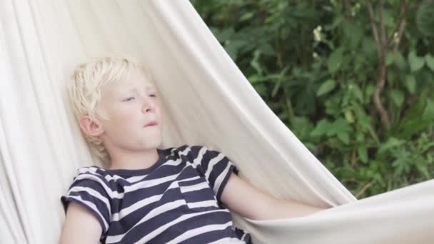 Lycklig blond pojke ligger i en hängmatta — Stockvideo