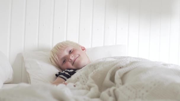 Snygg blond pojke ljuger på morgonen på sängen — Stockvideo