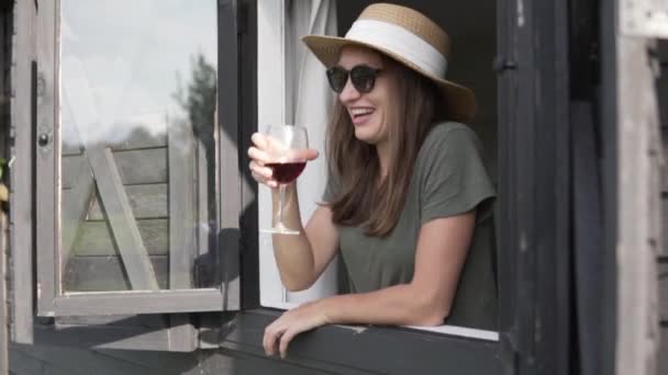 Η όμορφη γυναίκα με το καπέλο πίνει κόκκινο κρασί σε μια φάρμα.. — Αρχείο Βίντεο