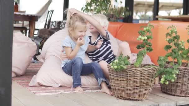 Милые брат и младшая сестра обнимаются на красивой веранде летом — стоковое видео