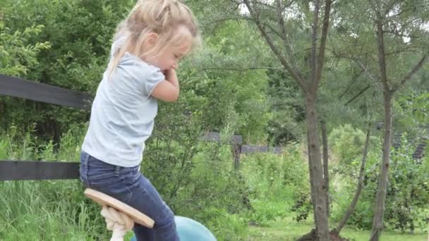 Kleines Mädchen reitet im Sommer auf einer Holzschaukel — Stockvideo