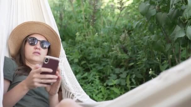 Žena v klobouku se houpá v houpací síti na farmě — Stock video
