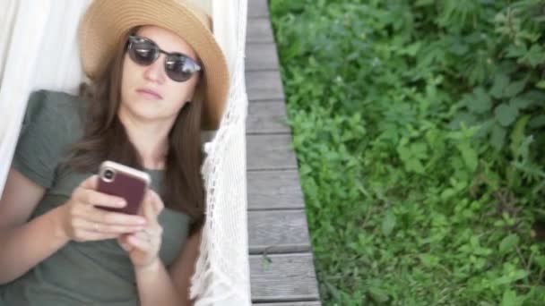Η γυναίκα με το καπέλο που ταλαντεύεται σε μια αιώρα το καλοκαίρι στο εξοχικό σπίτι — Αρχείο Βίντεο