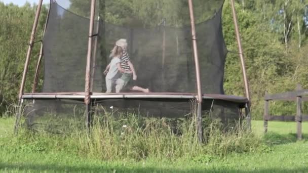 En gutt med en liten jente som hopper på en trampoline om sommeren i hytta. – stockvideo