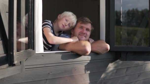 Vater und Sohn schauen aus dem Fenster und winken mit den Händen — Stockvideo