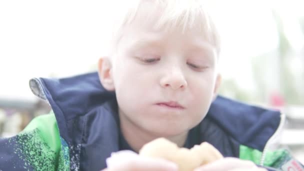 Голодный мальчик ест гамбургер на улице — стоковое видео