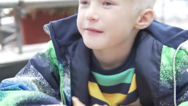Przystojny blond chłopiec chętnie zjada cheeseburger na ulicy jesienią — Wideo stockowe