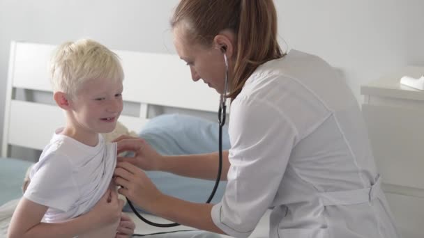 医者は診療所の少年に聴診器で耳を傾ける. — ストック動画