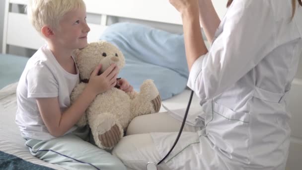 De arts luistert met een stethoscoop naar de patiënt en zijn teddybeer. — Stockvideo