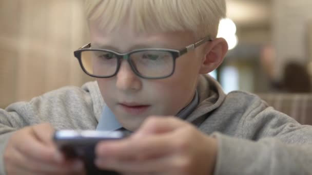 El chico con gafas mira cuidadosamente la pantalla de un teléfono móvil — Vídeos de Stock