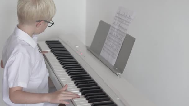 Der Junge spielt elektronisches Klavier auf Notenblättern — Stockvideo