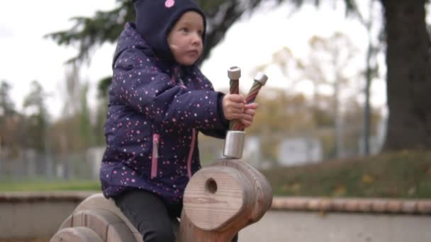 Liten flicka rider på en trägunga i parken på hösten. — Stockvideo