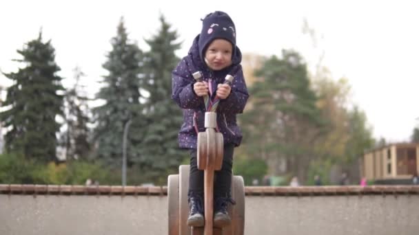 Een kind speelt in de speeltuin in de herfst in het park — Stockvideo