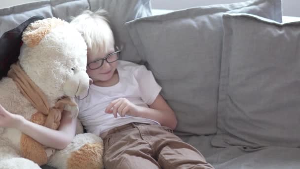 Mooie jongen schooljongen speelt thuis met een teddybeer — Stockvideo