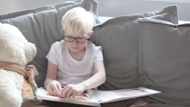 A blond boy is looking at his childrens photo album — Stock Video