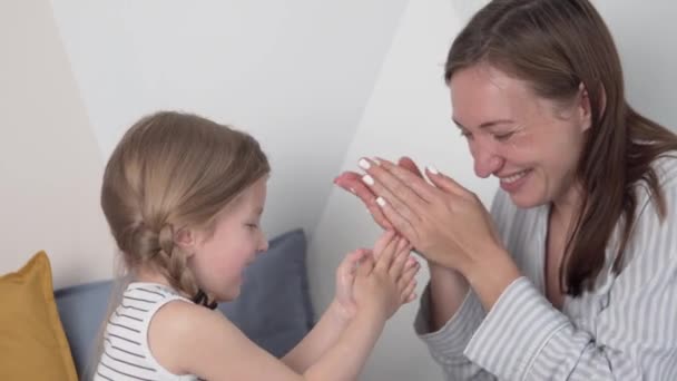 Mutter und kleine Tochter tragen fröhlich Creme auf Körper und Gesicht auf — Stockvideo