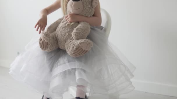 Vestida niña se sienta en una silla con un oso de peluche — Vídeos de Stock