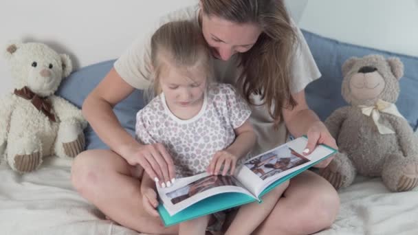 Mamá muestra a su hija una foto en el álbum de fotos en casa — Vídeos de Stock