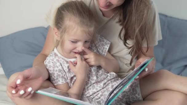 Mutter und kleine Tochter betrachten schöne Samenfotos im Fotoalbum des Hauses auf dem Bett — Stockvideo