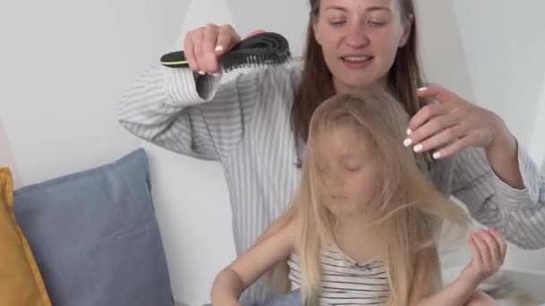 Uma mulher penteia o cabelo comprido do pente de sua filhinha — Vídeo de Stock