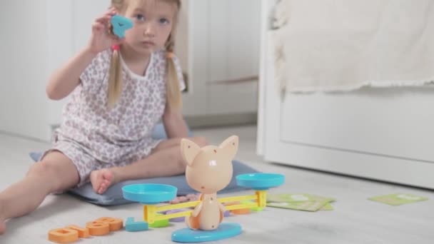 Een klein meisje bestudeert de samenstelling van het aantal in het spel van gewichten met getallen — Stockvideo