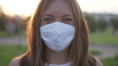 Güneş batarken bir yaz parkında tıbbi maske takan güzel bir kadının yakın çekimi.