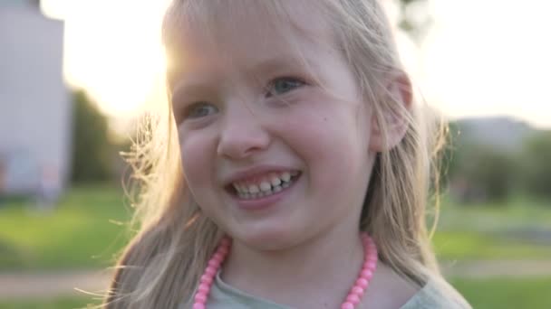 Nahaufnahme eines lachenden kleinen Mädchens inmitten eines Sonnenuntergangs in einem Sommerpark — Stockvideo
