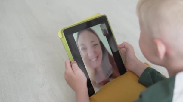 De blonde jongen spreekt op een tablet via video link met zijn moeder — Stockvideo
