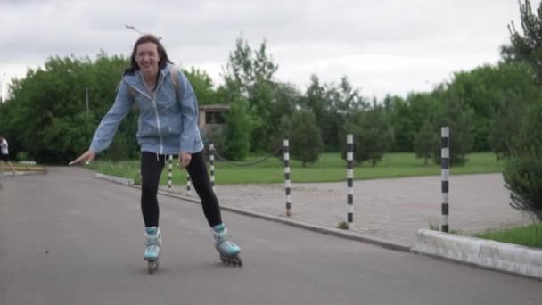 Beautiful woman brunette rides on rollers on camera and waves her hand — Stock Video