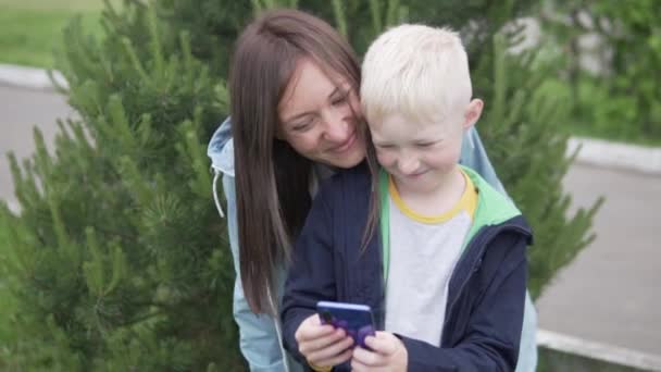 En mor och hennes tonåriga son tar en selfie på en mobiltelefon på en promenad i parken — Stockvideo