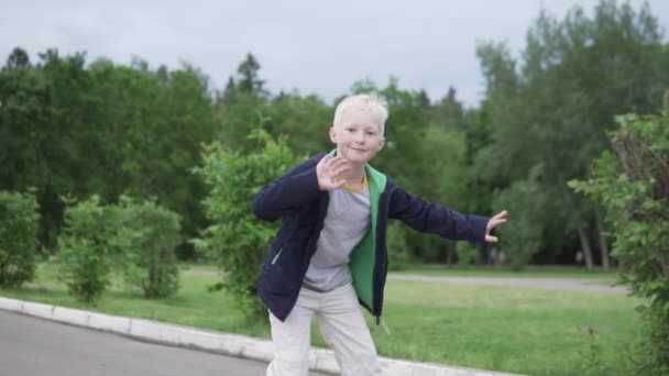 Lindo menino loiro monta em rolos e acena sua mão — Vídeo de Stock