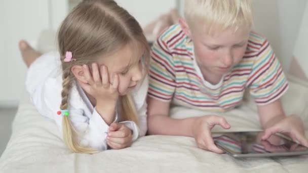 Leuke kinderen broer en zus spelen in de tablet thuis op de rand in de kinderkamer — Stockvideo