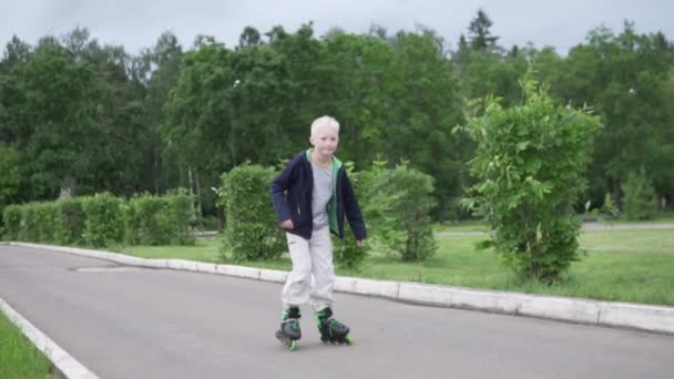 Een jonge jongen leert rolschaatsen in een park. — Stockvideo