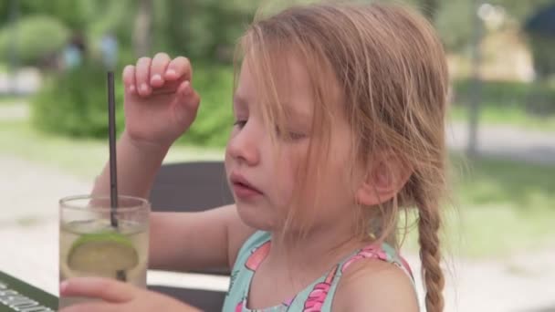 En liten flicka äter is från lemonad en varm sommardag på ett café — Stockvideo