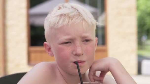 Moe van de hitte drinkt de blonde jongen koude limonade aan een tafel in het café. — Stockvideo