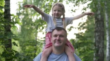 Güzel küçük bir kız gün batımında ormanda yürürken babasının omuzlarında oturur..