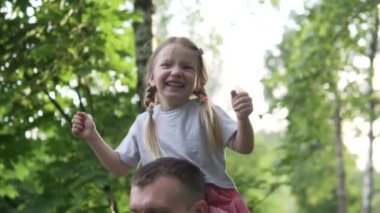 Güzel küçük bir kız yaz yürüyüşü sırasında babasının omuzlarında oturur.