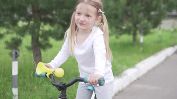 Ένα μικρό κορίτσι βουίζει σε ένα χαβαλέ σε ένα ποδήλατο κατά τη διάρκεια μιας ποδηλασίας στο πάρκο το καλοκαίρι — Αρχείο Βίντεο