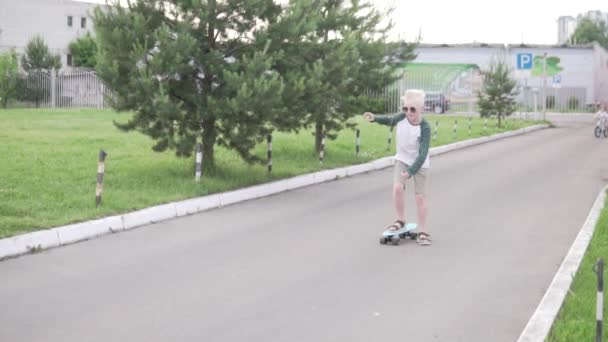 En blond pojke lär sig åka skridskor i en park på sommaren — Stockvideo