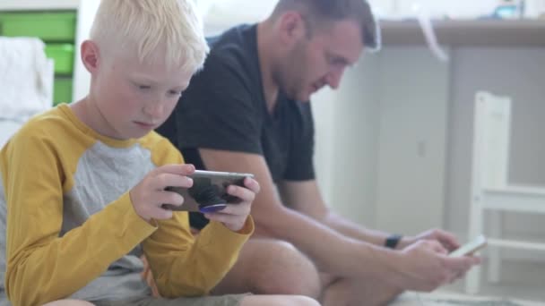 Papa en zoon spelen spelletjes op de mobiele telefoon thuis op de vloer. — Stockvideo