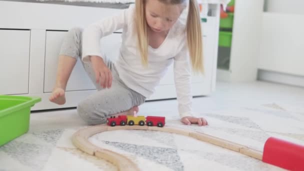 Una hermosa niña juega un ferrocarril de madera en un juguete — Vídeos de Stock