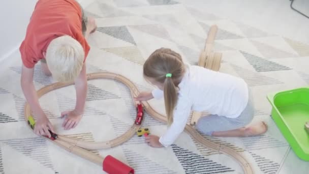 Crianças bonitas jogar o jogo de madeira ferroviária em casa durante o auto-isolamento — Vídeo de Stock